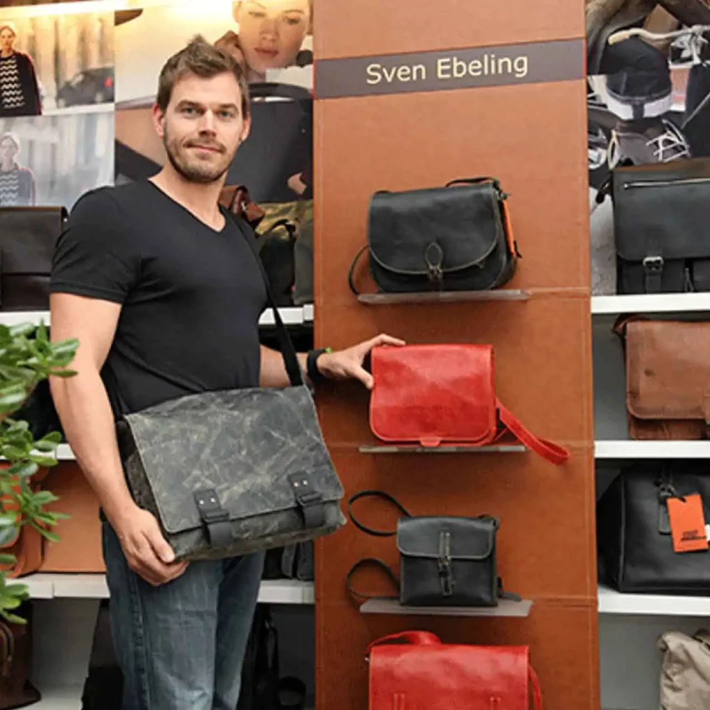 Lederwaren by Sven Ebeling - Die Adresse für erstklassige Accessoires, Taschen, Koffer und mehr in Magdeburg - Inhaber Sven Ebeling vor einem Taschenregal in seinem Ladengeschäft